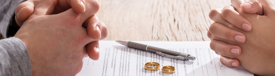 hands of divorcing couple on top of divorce papers with wedding rings in the middle