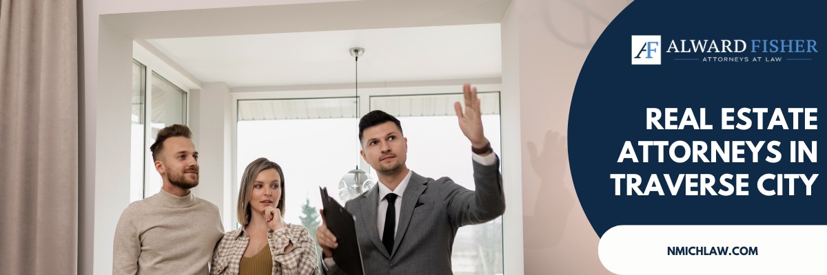 A Traverse City real estate attorney in a suit gestures upward while advising a couple inside a property with large windows.